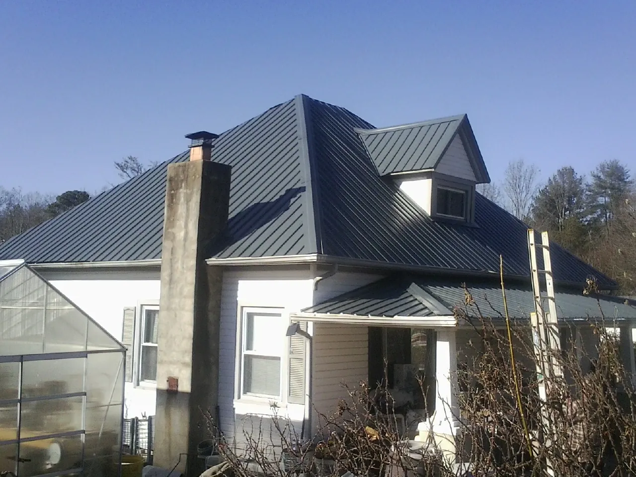 Dark blue standing seam metal roof on a white farmhouse with dormer — Slate & Tile Roof Repair by Roofing Brothers in Menifee