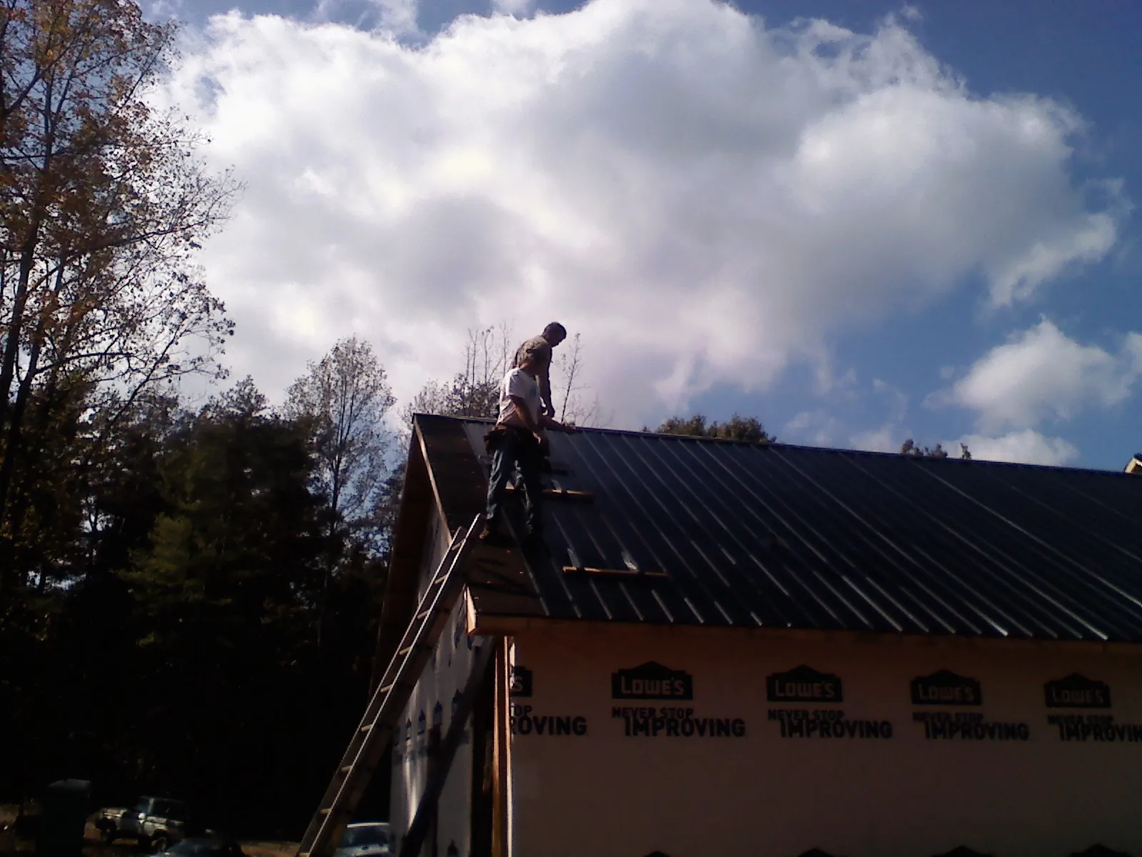 Roofer fastening dark metal panels high against a cloudy sky, from a Roof Inspection job in Menifee